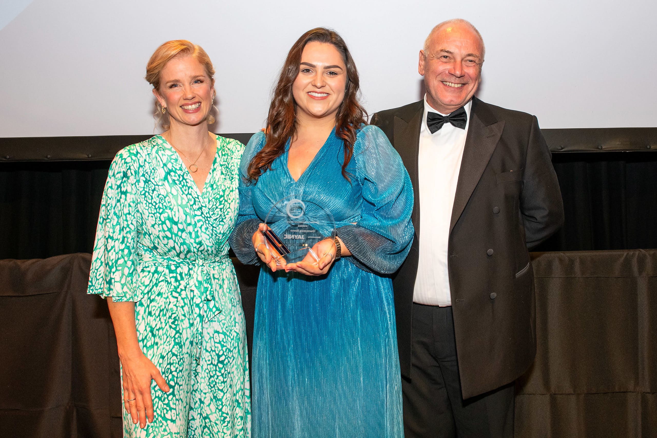 Three people, one holding an award